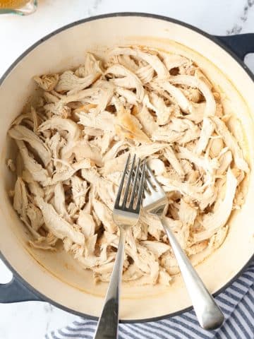 A Dutch Oven with two forks and shredded chicken.