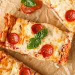 A rectangular slice of pizza topped with pepperoni and basil.