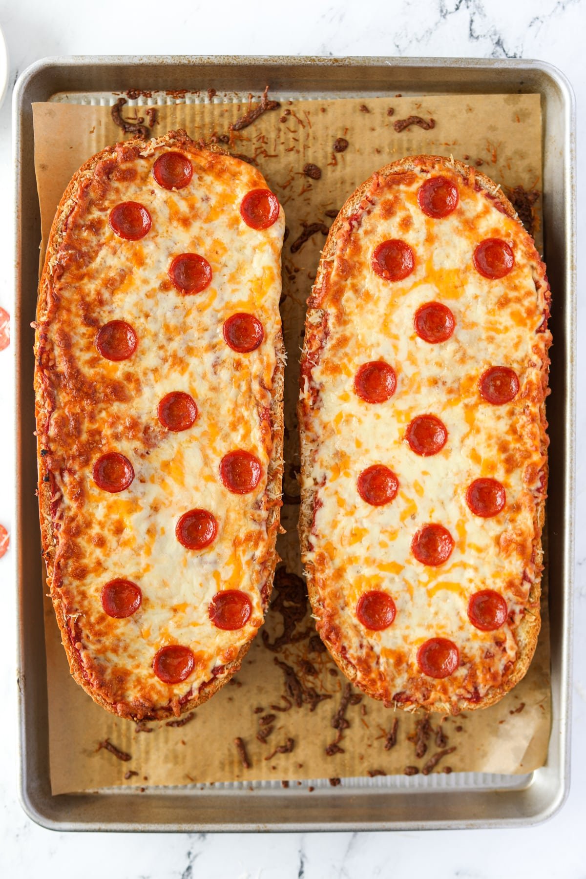 Two halves of French Bread pizza on a baking sheet.