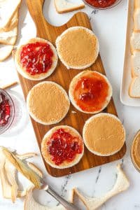 Spreading jam and jelly on top of peanut butter coated bread slices.