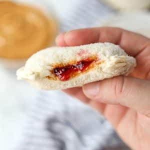 A hand holding a round peanut butter and jelly sandwich.