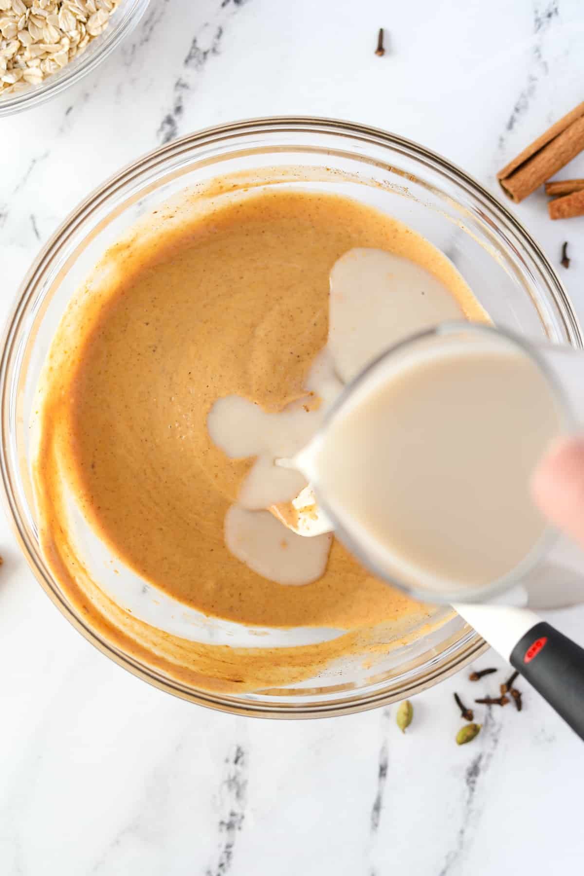 Adding cashew milk to a bowl full of pumpkin colored liquid.