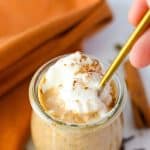 A spoon taking a portion of pumpkin oats in a jar, topped with whipped cream.