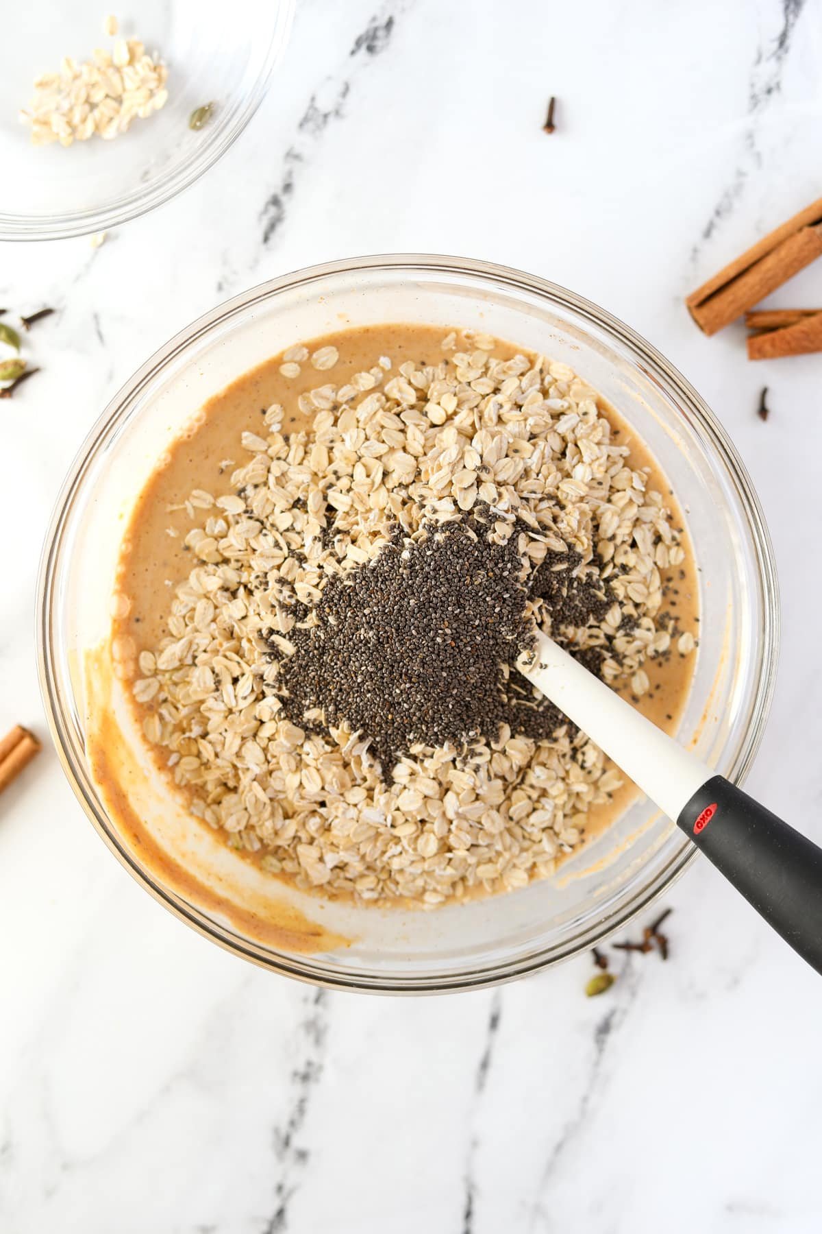 Adding oats and chia seeds to a bowl of pumpkin colored liquid.