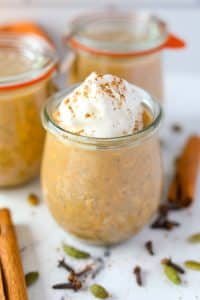 A jar of overnight oats, garnished with whipped cream and a pinch of pumpkin spice on top.