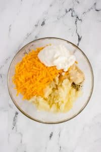 A bowl with mashed potato, cheese, sour cream, and spices.