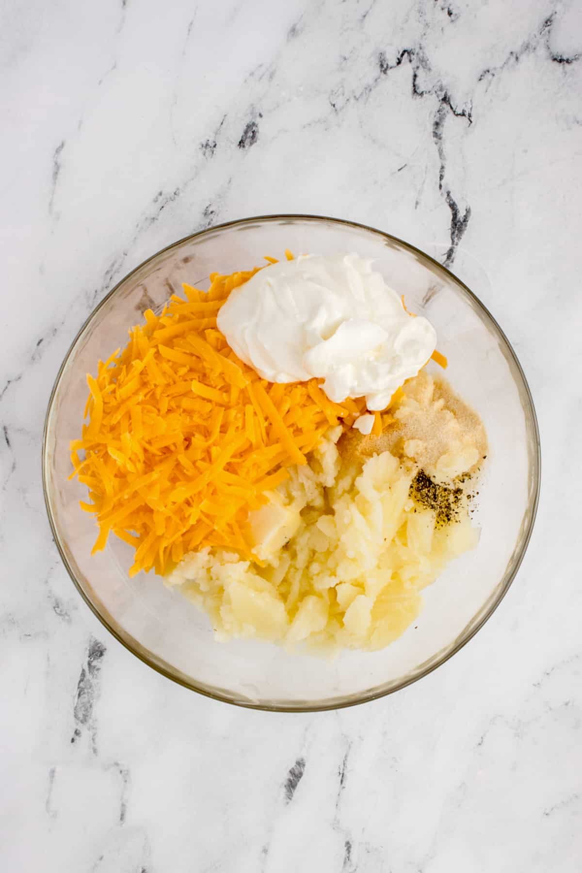 A bowl with mashed potato, cheese, sour cream, and spices.