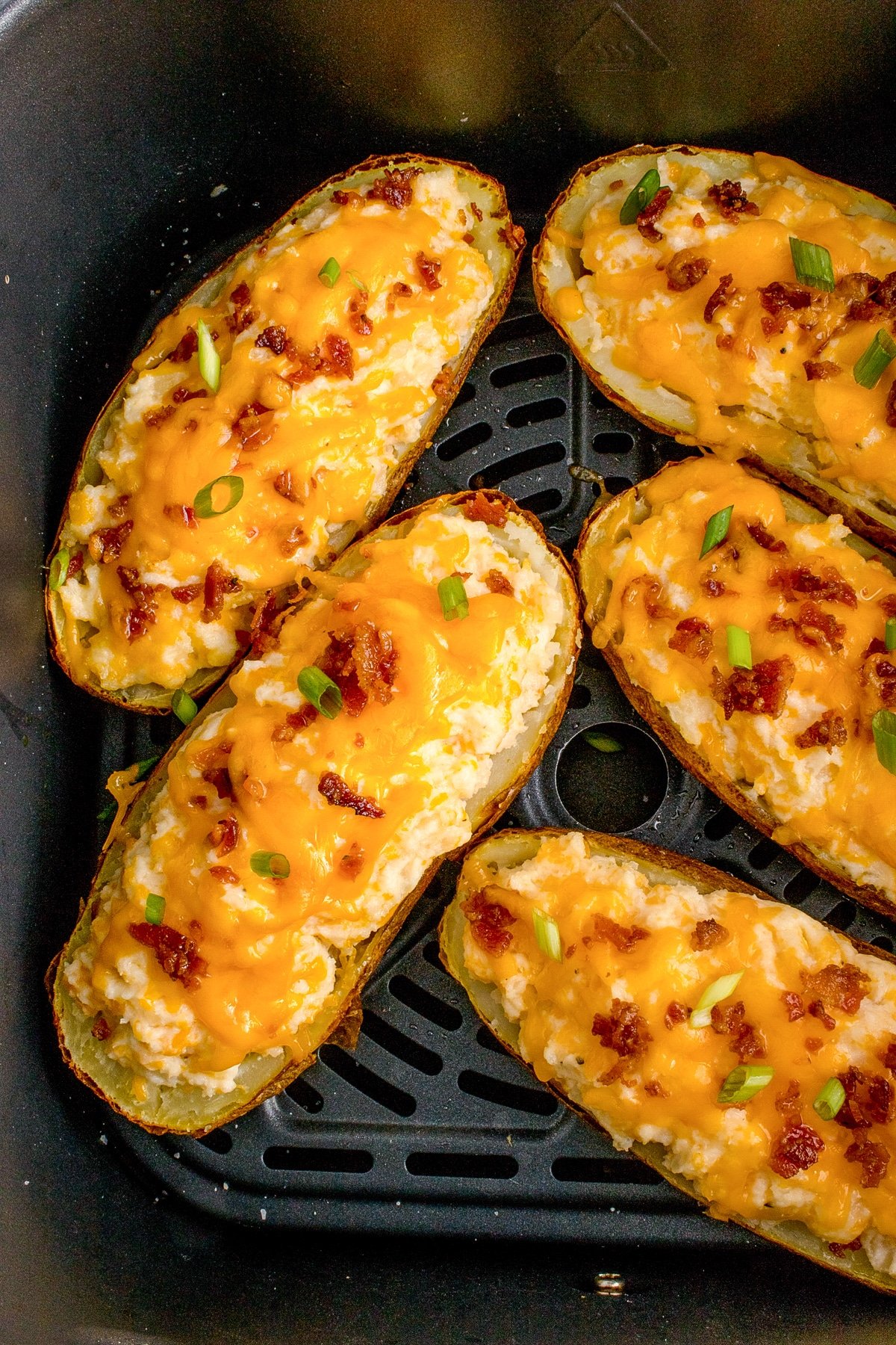 An air fryer basket filled with 5 potato halves filled with a cheesy and bacon topped filling.