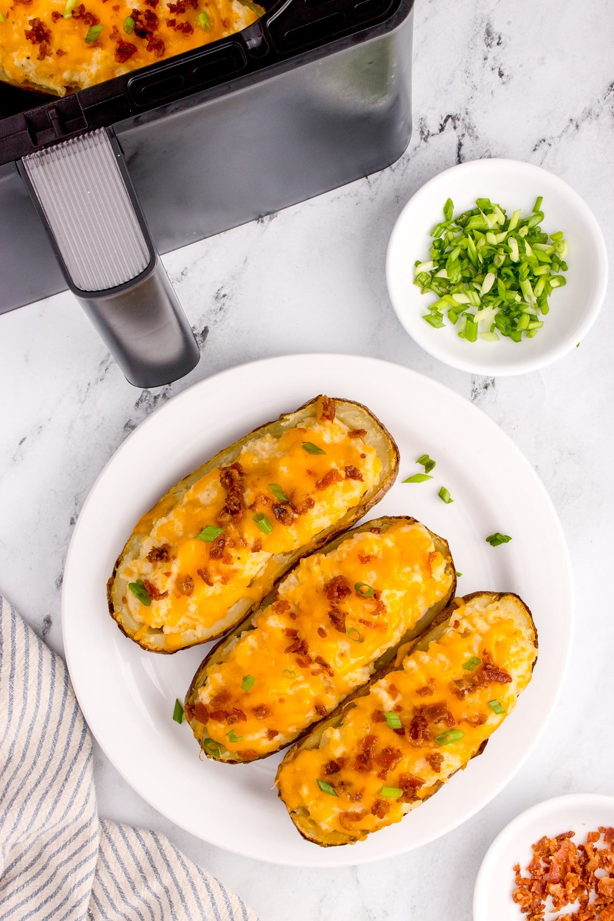 Three stuffed potatoes on a plate, with an air fryer in the background.