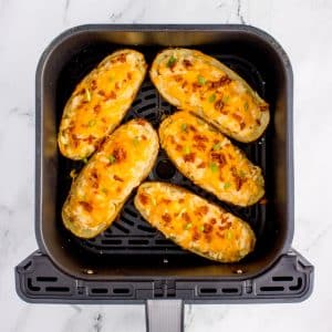 An air fryer basket filled with loaded twice-baked potato halves.