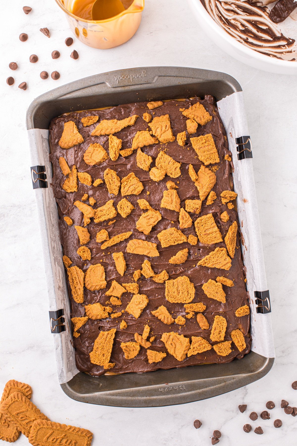 A baking pan filled with brownie batter and topped with cookie pieces.