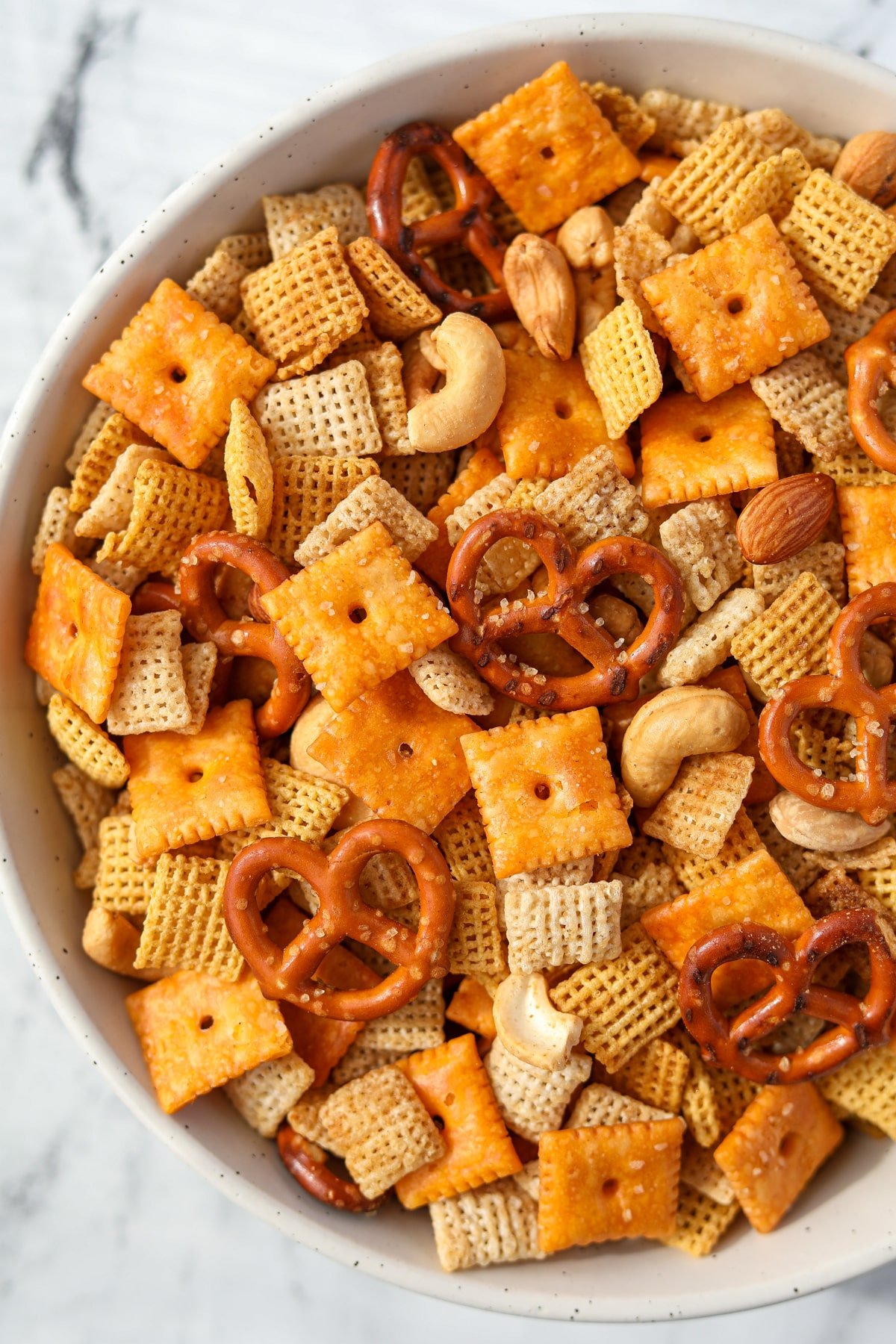 An overhead view of a bowl of snack mix with pretzels, crackers, cereal, and nuts.