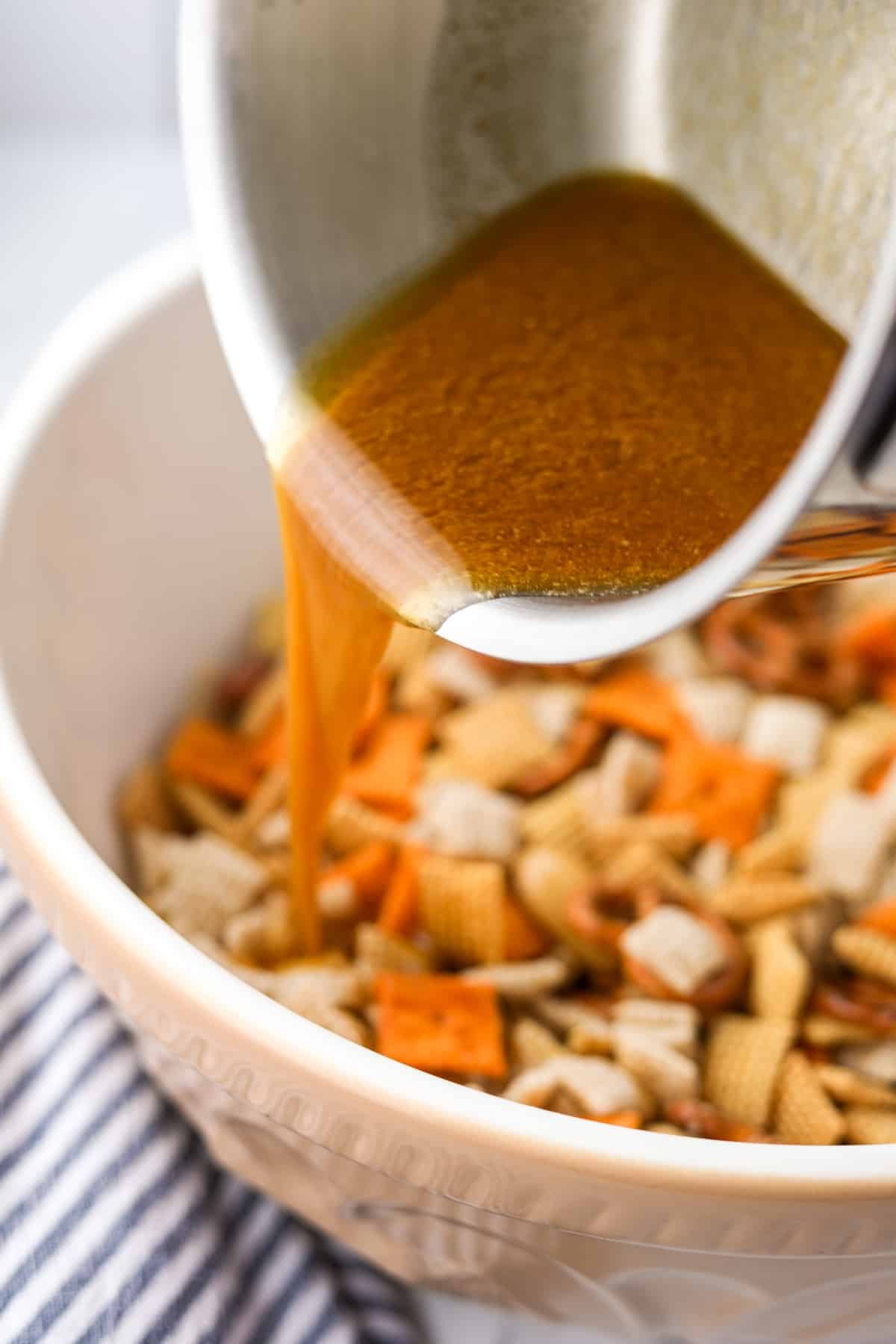 Pouring melted butter into a bowl of snack mix.