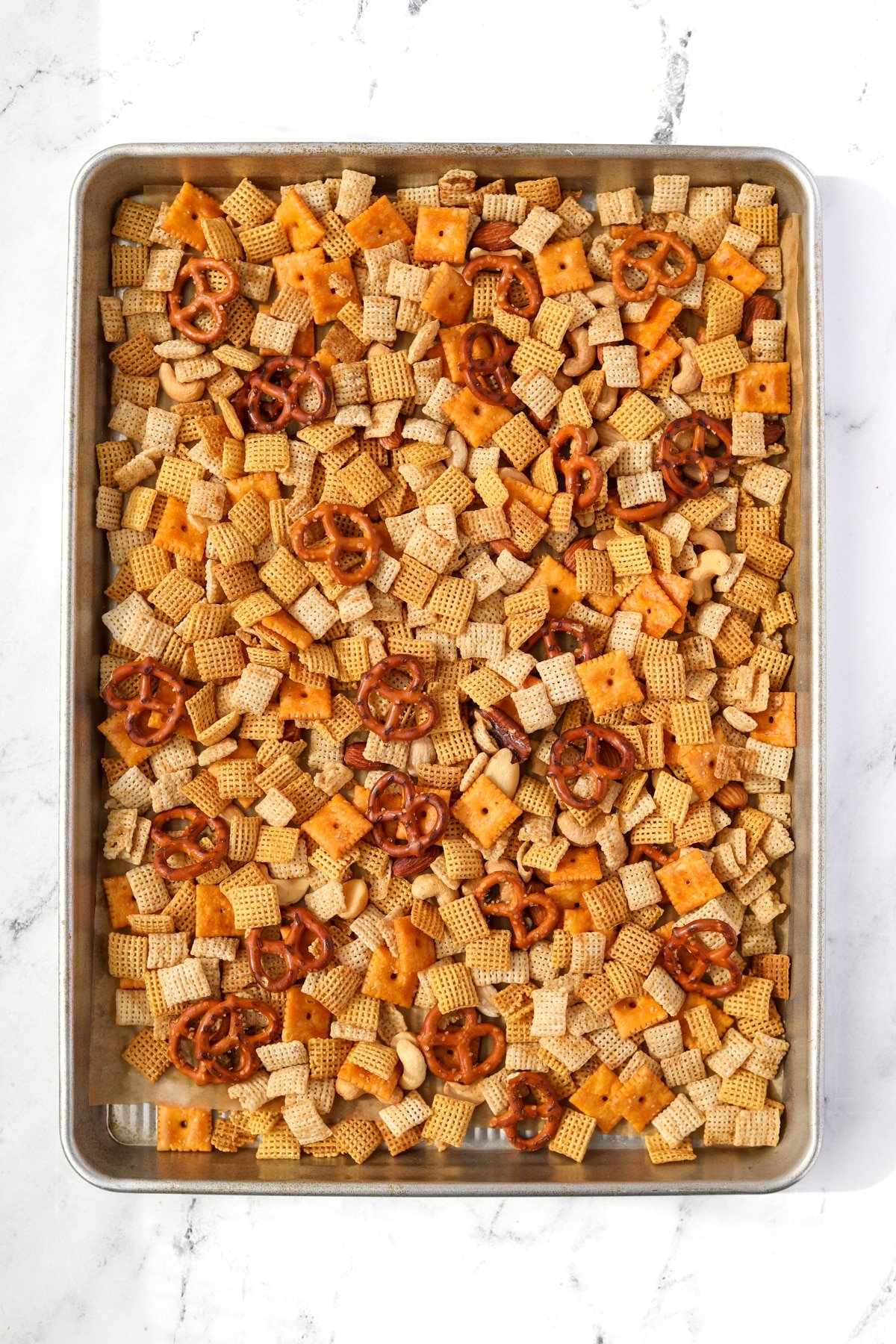 A baking sheet filled with snack mix with pretzels, cereal, and crackers.