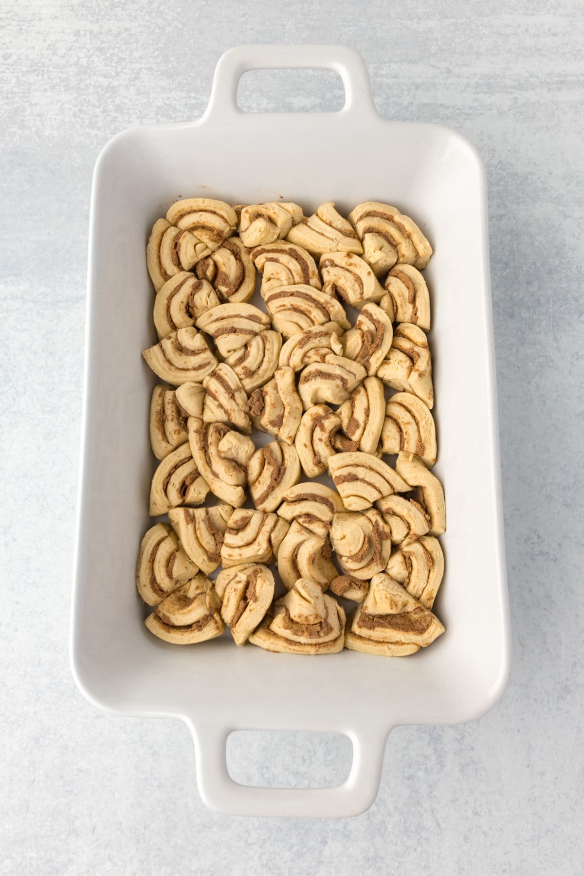 A casserole dish with cinnamon rolls sliced and fit into the dish in an even layer.