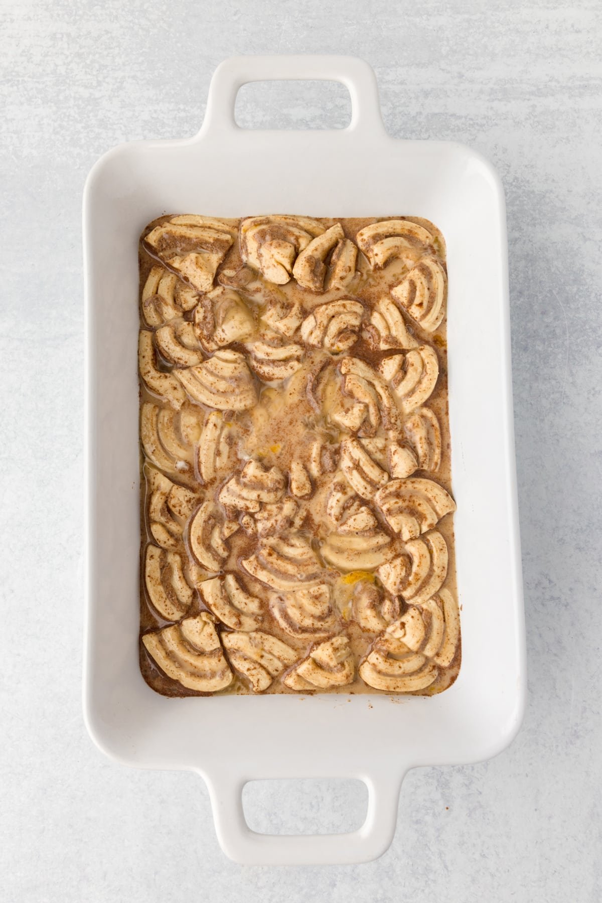 A baking dish with sliced cinnamon rolls and a custard base in it.