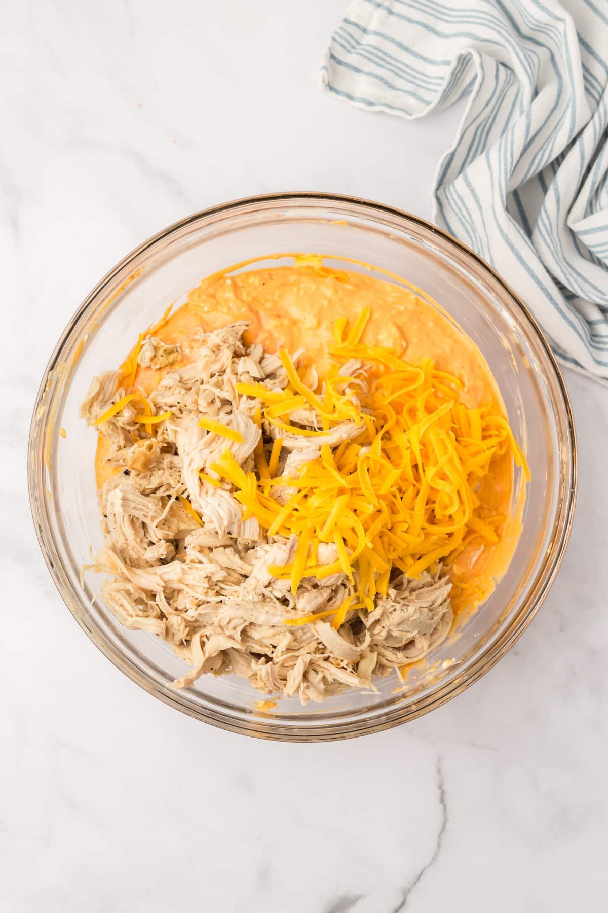 A bowl filled with a dip mixture, with shredded cheese and cooked chicken on top.