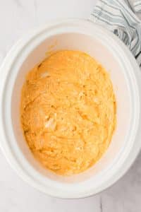 A white crock pot filled with a cheesy chicken dip.