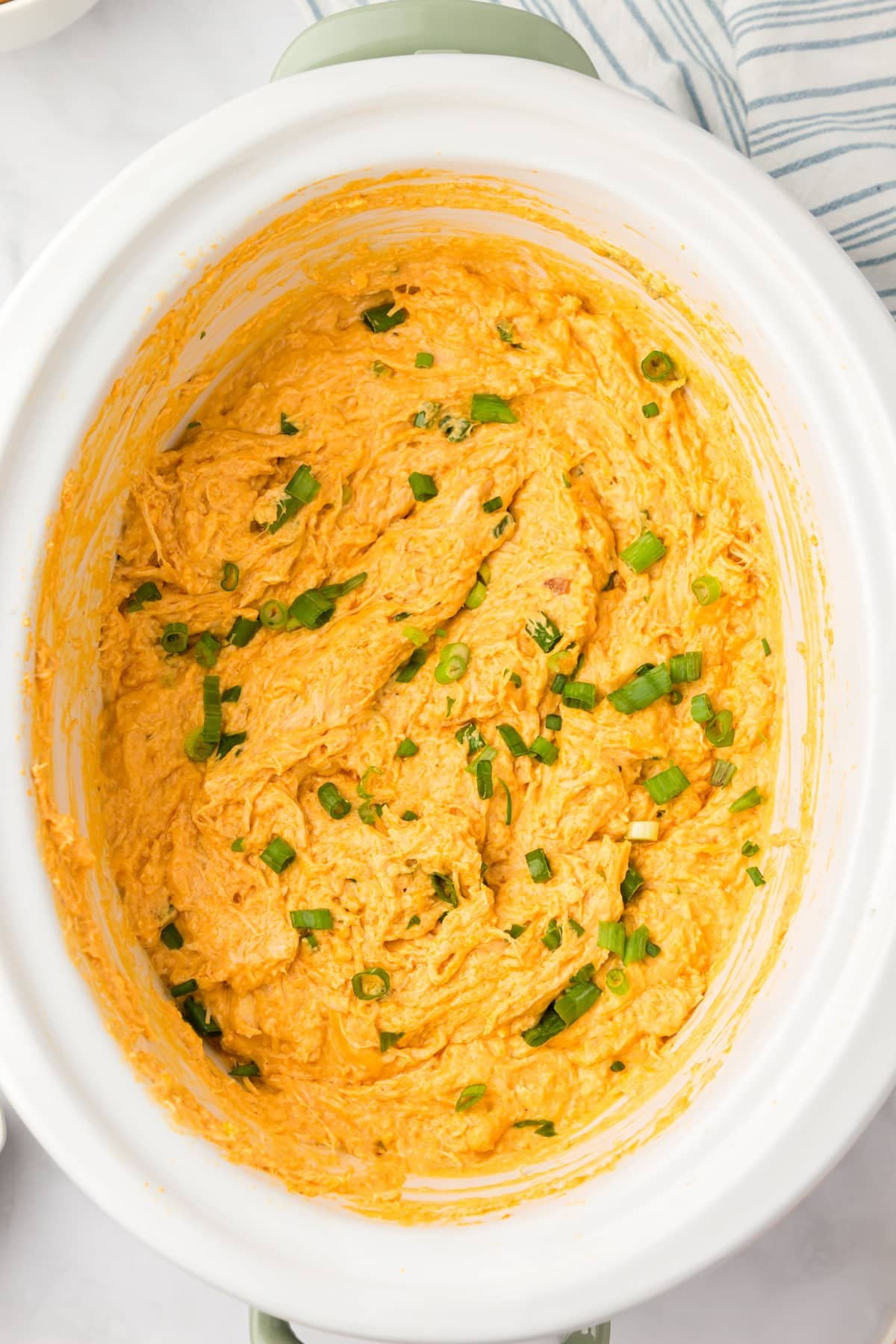 A white crock pot with a cheesy chicken dip inside.