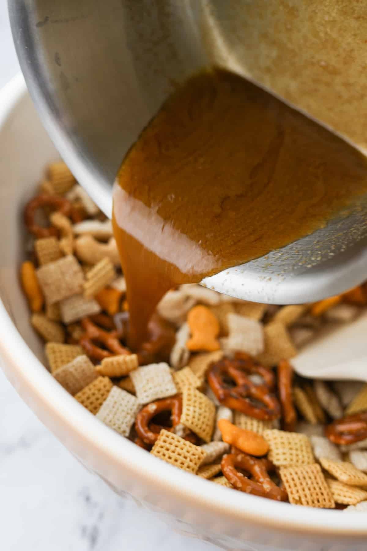 Pouring butter and seasonings over a dry snack mix in a large bowl.