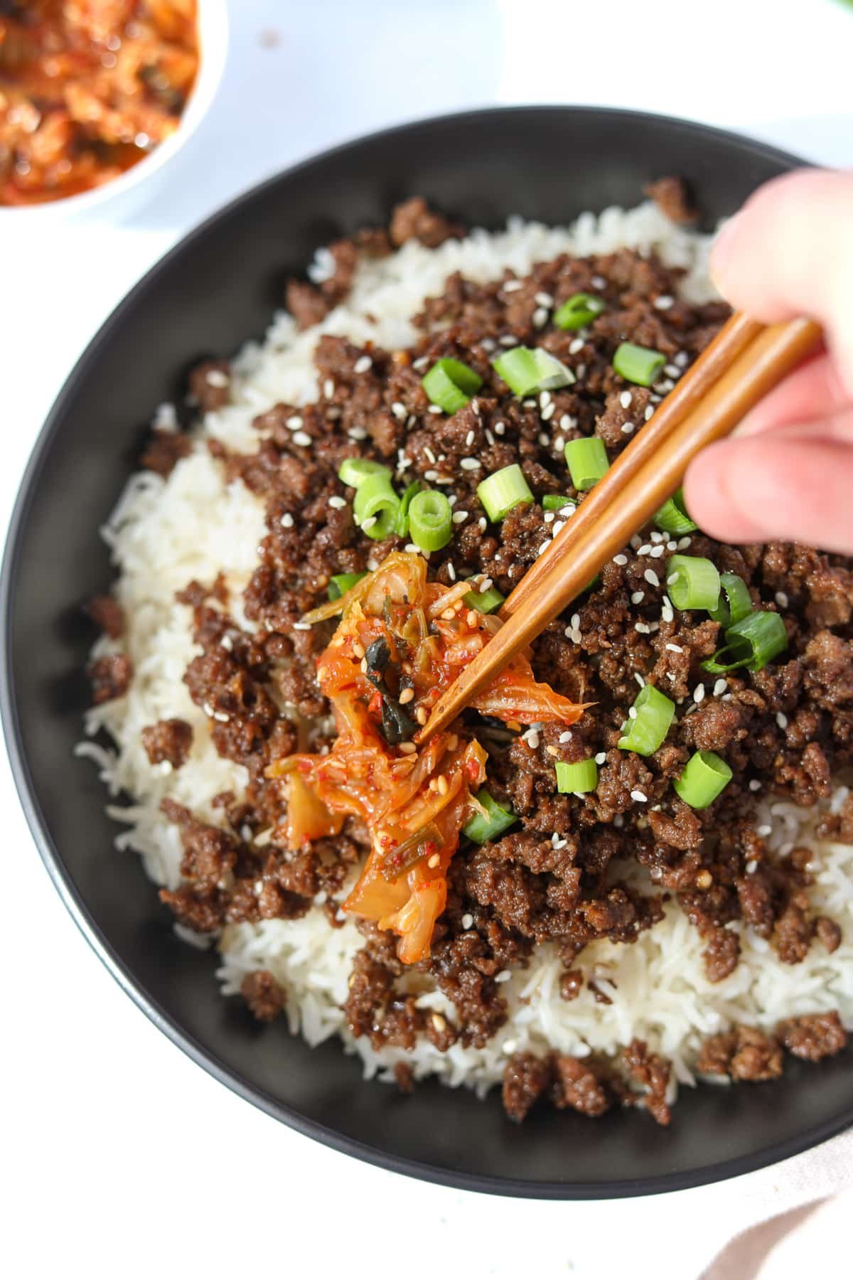 Placing a piece of kimchi on a bowl of Korean beef and rice.