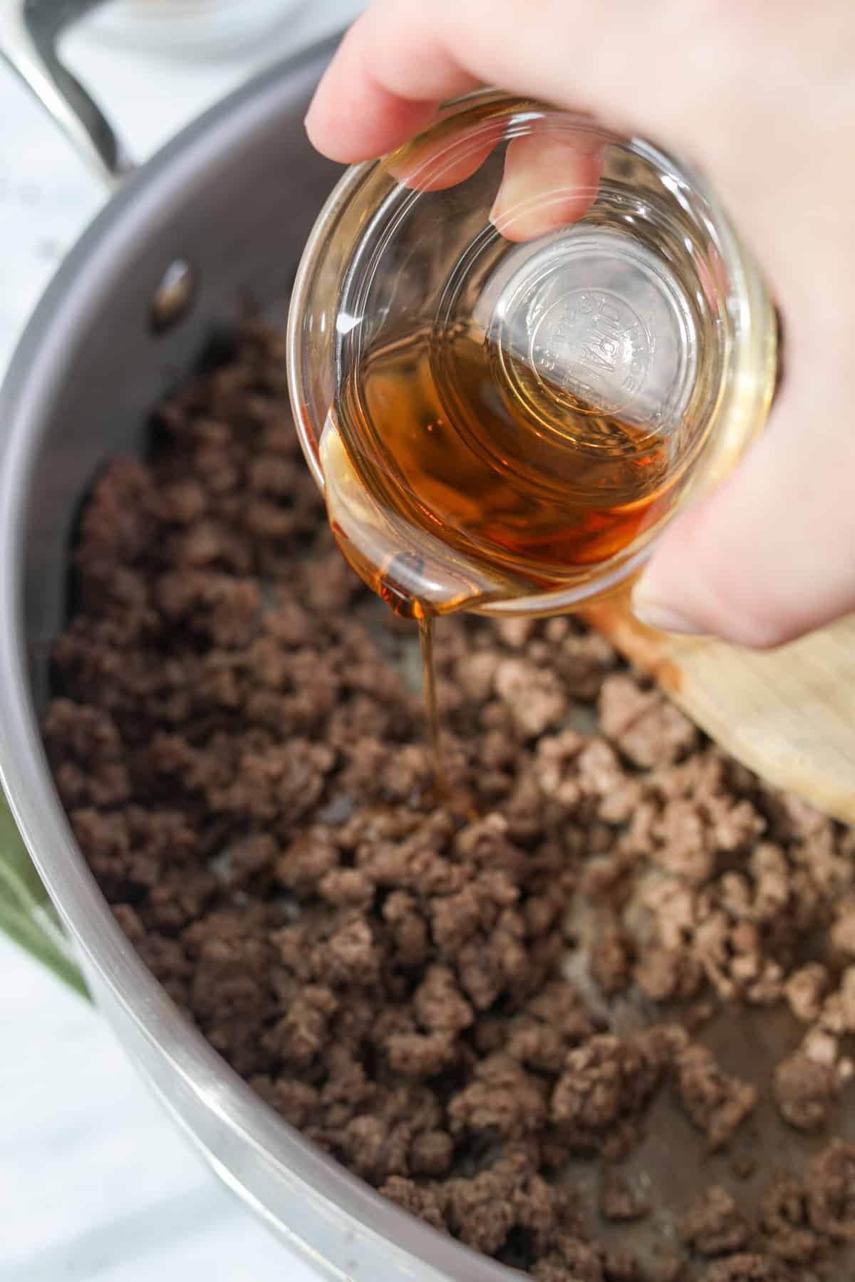 Drizzling sesame oil into a skillet with cooked ground beef.