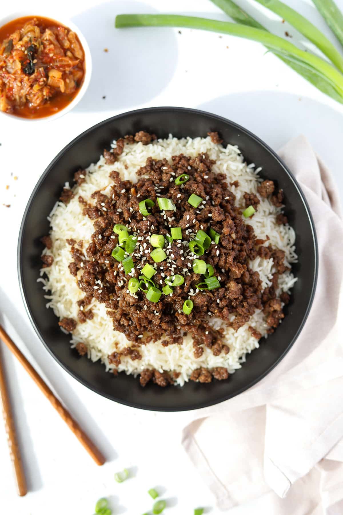 A bowl filled with rice and topped with seasoned ground beef, green onions, and sesame seeds.