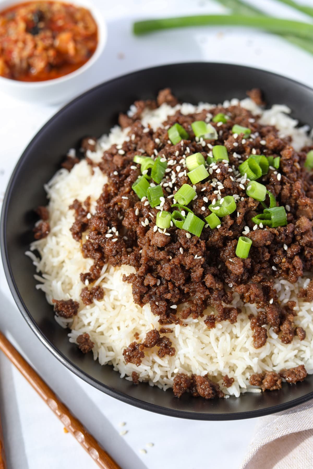 A bowl of rice topped with Korean ground beef, green onions, and sesame seeds.