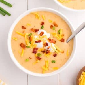A bowl of cheesy soup topped with sour cream, cheese, and bacon.