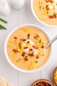 A bowl of cheesy potato soup, garnished with sour cream, bacon, cheese and chives.