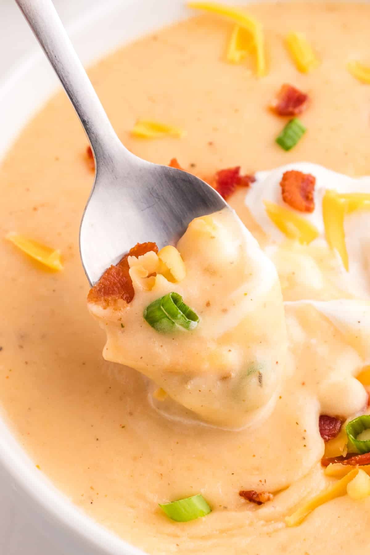 A spoon taking a portion of potato soup, garnished with green onions and bacon.
