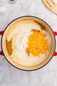A Dutch Oven with a pureed soup, with sour cream, heavy cream, and shredded cheese added.