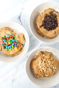 Three bowls of cookie dough, with three different mix-ins: chocolate chips, m&ms, and peanuts.