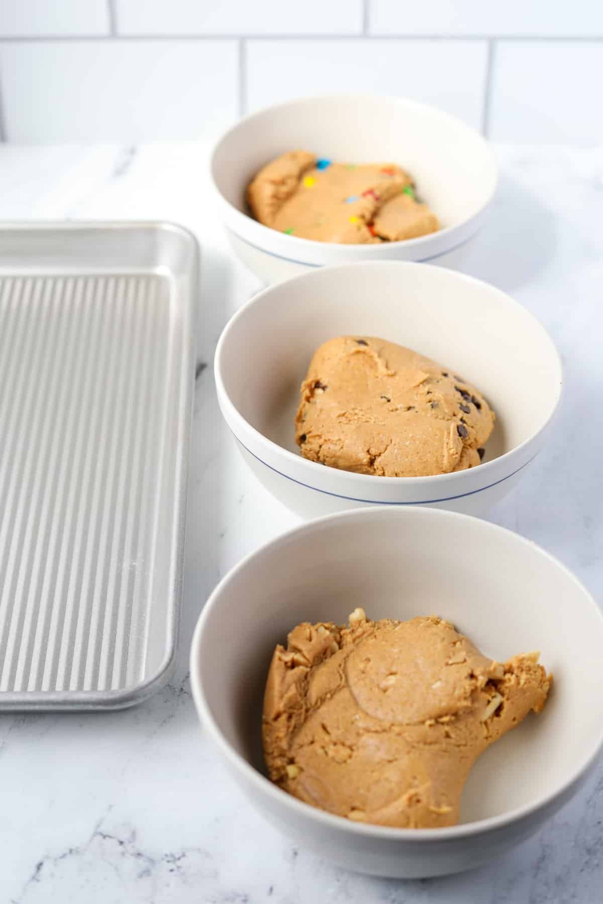 Three bowls of dough resting next to a baking sheet.