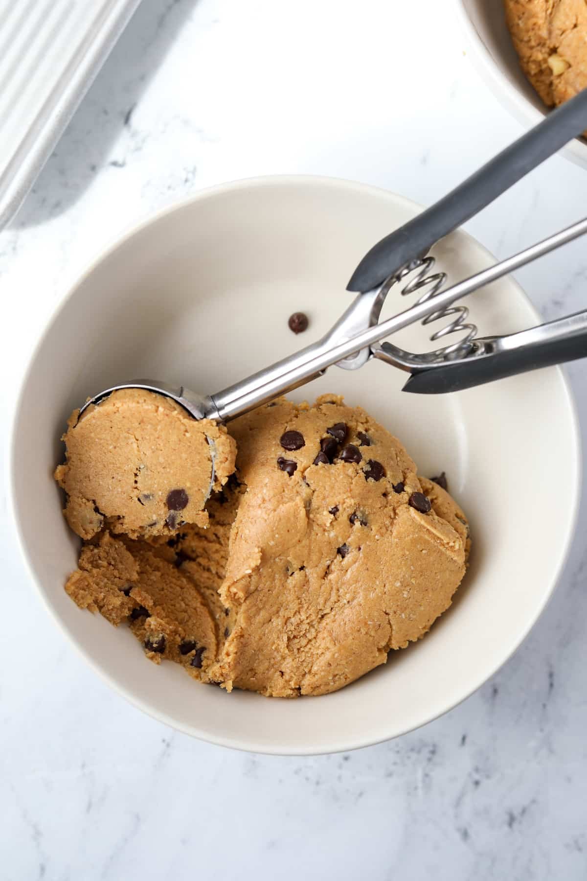 A bowl with protein cookie dough being scooped by a cookie scoop.