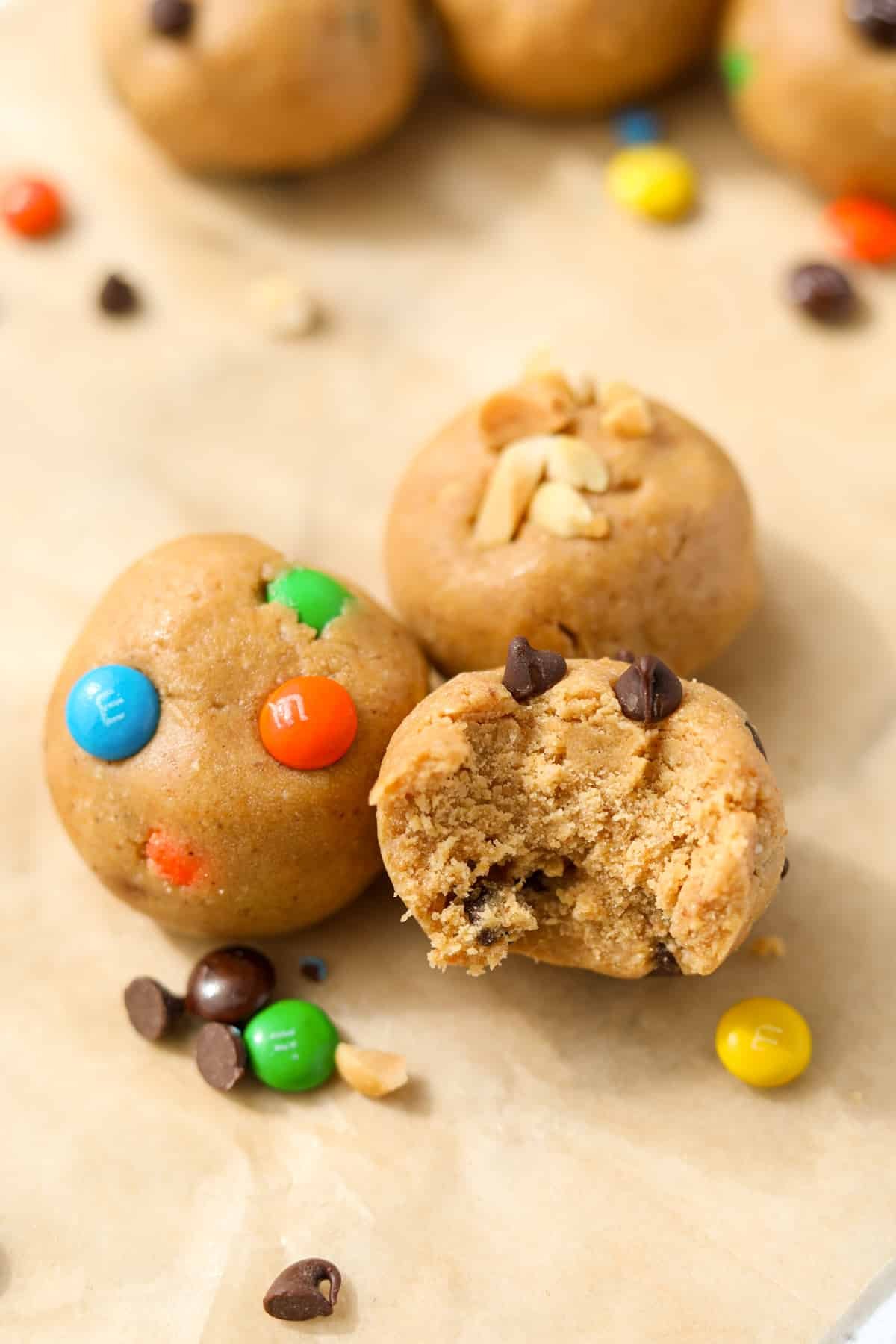 Three cookie dough balls featuring m&m's, chocolate chips, and chopped peanuts.