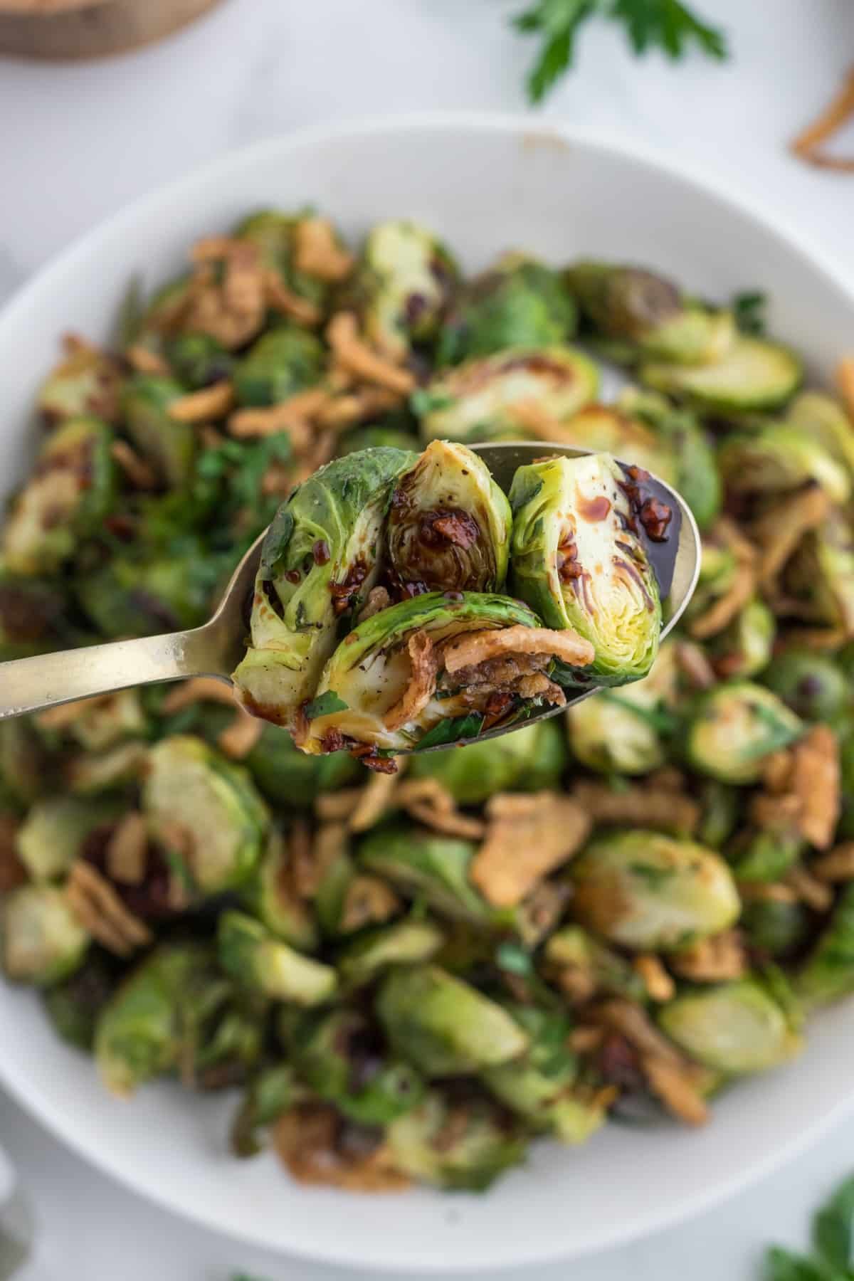 Lifting a spoon full of crispy brussels sprouts from a platter.