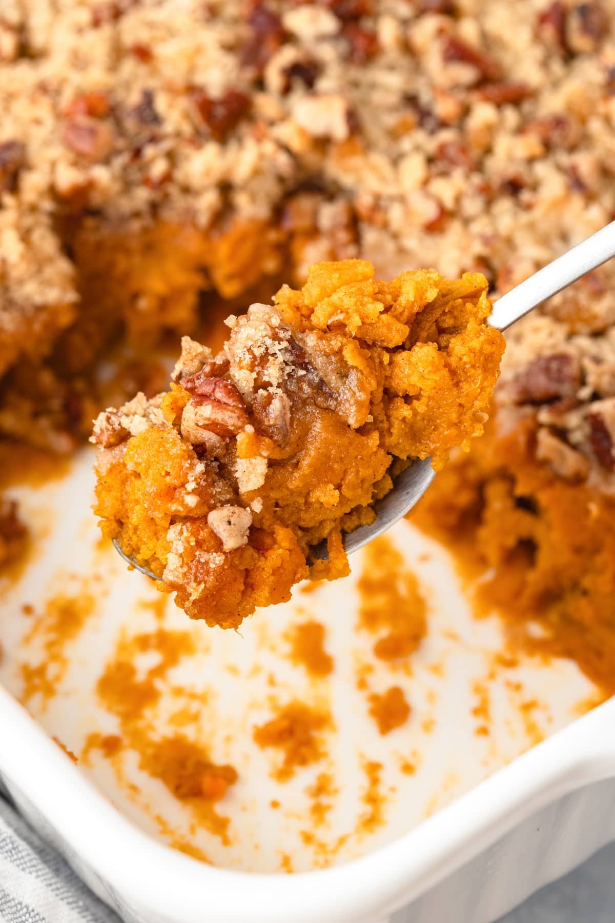A spoon taking a portion of sweet potato casserole with pecans.