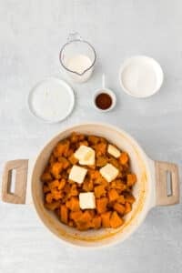 A pot filled with cooked sweet potatoes and a few pats of butter.