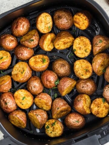 An air fryer basket filled with baby potato halves.