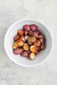 A bowl of red potatoes topped with olive oil and seasonings.
