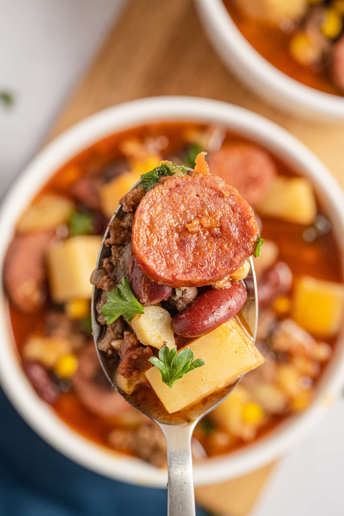 A spoon with Southwestern stew on it, including a smoked sausage round and kidney beans.