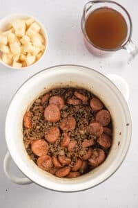 A soup pot filled with ground beef and sliced sausages.