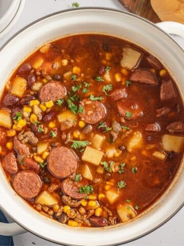 A large pot filled with ground beef stew with sliced sausages.
