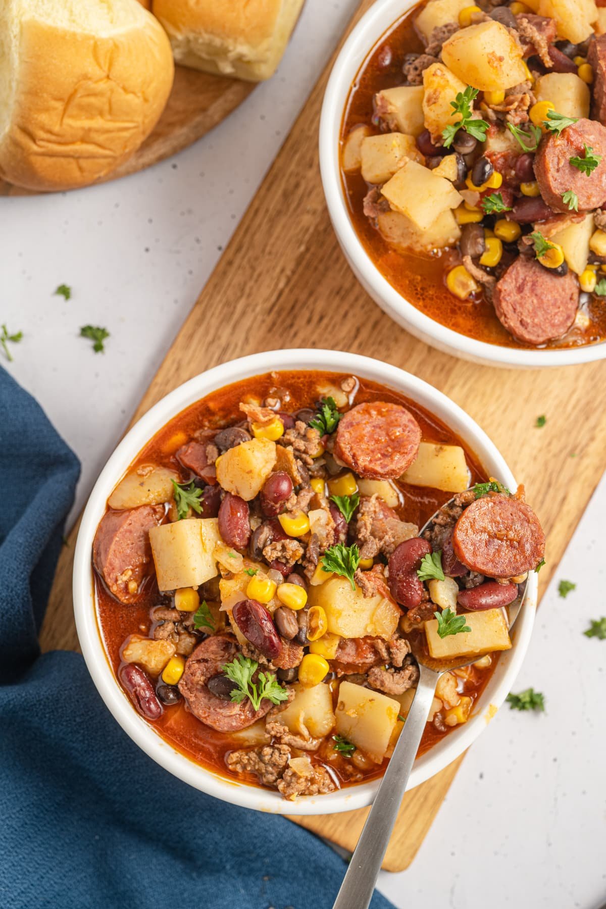 An overhead view of two bowls of hearty soup, containing ground beef, potatoes, and corn.