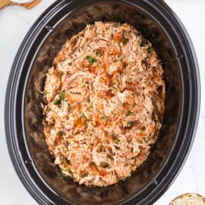 A slow cooker filled with shredded chicken that has been cooked in salsa.