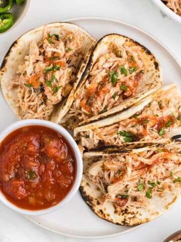 A plate of four folded chicken tacos, with a side of salsa in a small bowl.