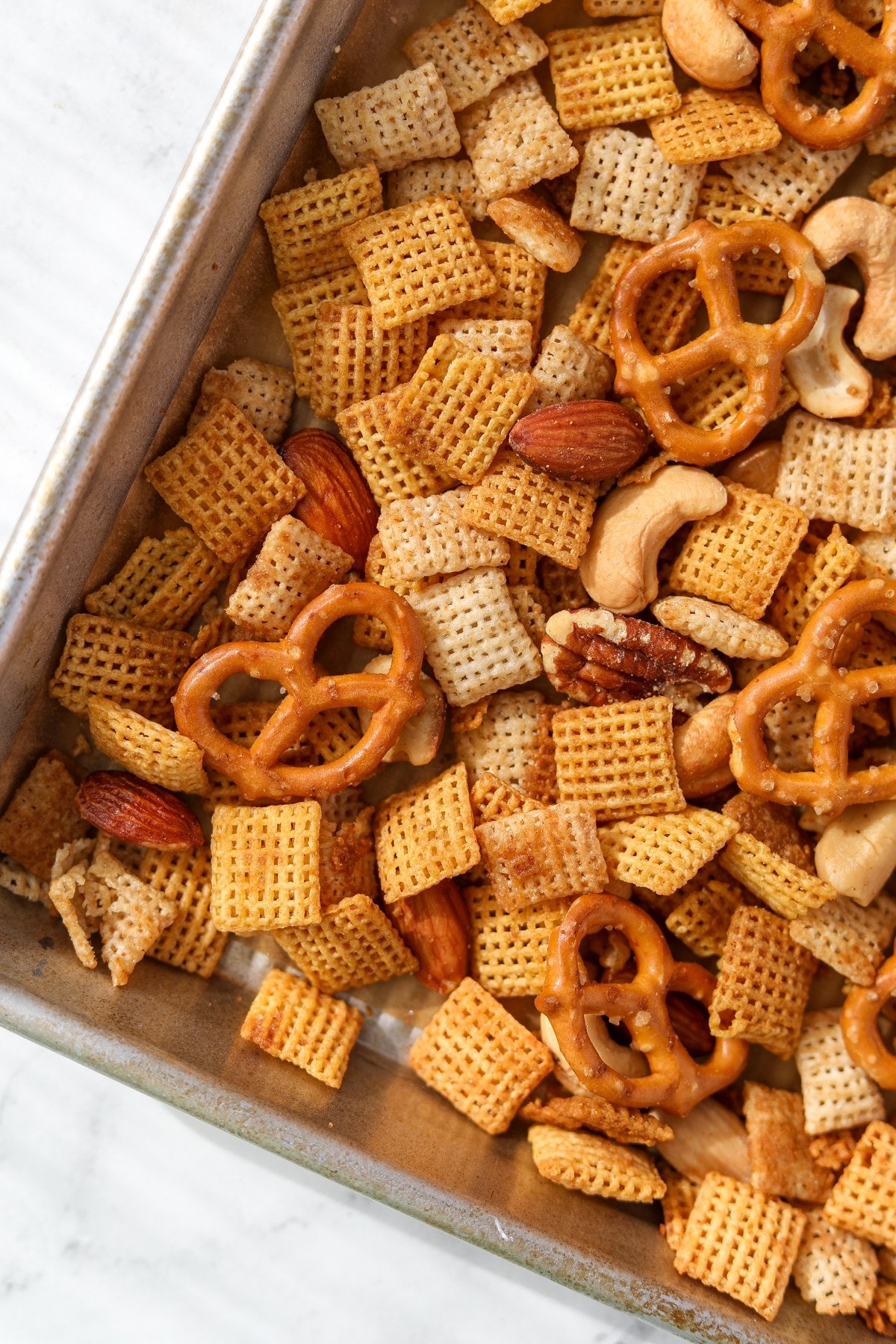 A baking sheet with chex mix featuring pretzels and mixed nuts.