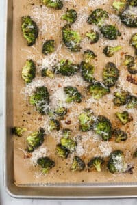 Roasted broccoli on a baking sheet topped with parmesan cheese.