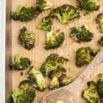 A baking dish with roasted broccoli, and a wooden spoon scooping a portion for serving.
